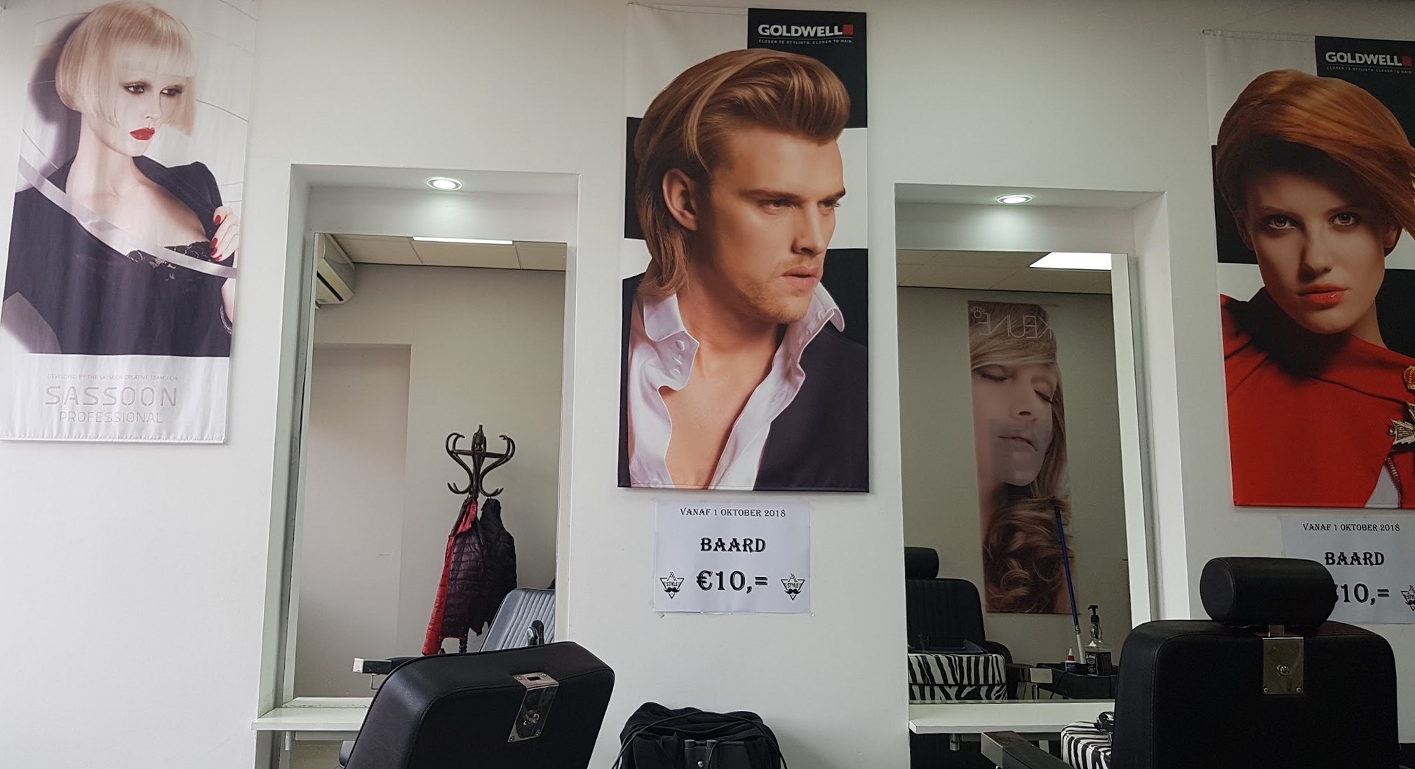 De achterwand van de zaak met grote posters van kapsels, zwarte stoelen en een prijsbordje